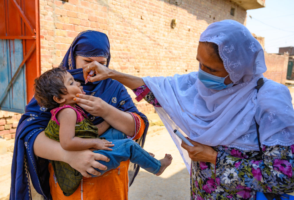 On 23 July 2020 in Faisalabad, Punjab, Pakistan, polio staff Razia Bano, age 48, marks the finger of an eight-month-old boy after he’s received the polio vaccine, as he sits in his mother’s lap.