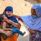 On 23 July 2020 in Faisalabad, Punjab, Pakistan, polio staff Razia Bano, age 48, marks the finger of an eight-month-old boy after he’s received the polio vaccine, as he sits in his mother’s lap.